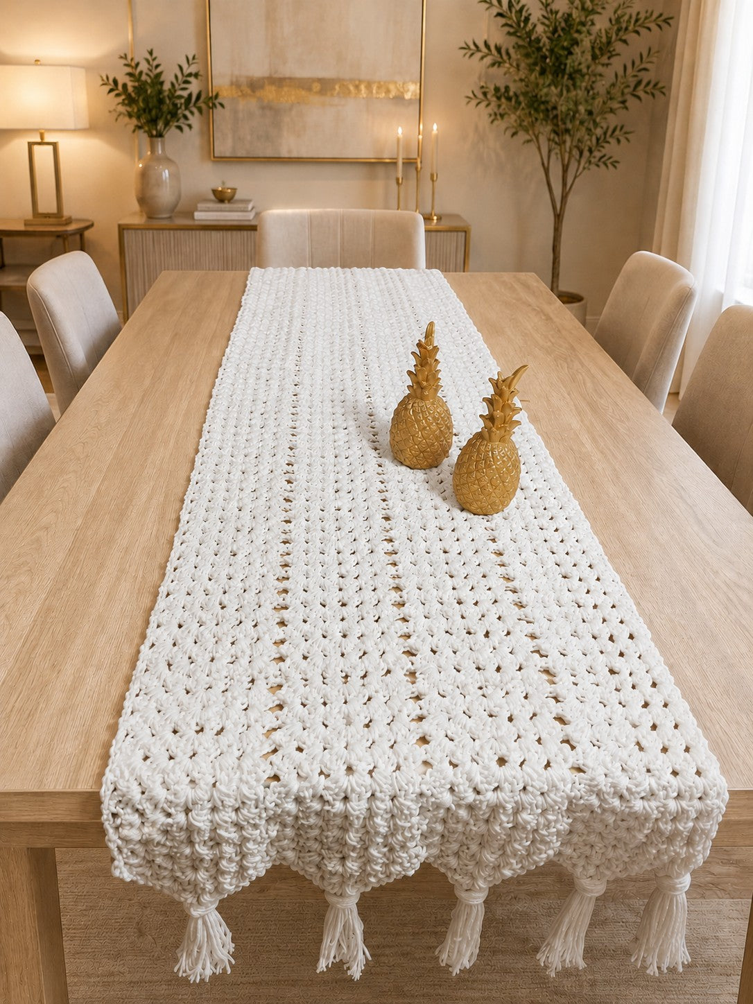 Ovela off-white textured crochet table runner with decorative gold pineapple accents and tassels.
